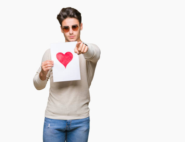 istock Young handsome man holding card with red heart over isolated background pointing with finger to the camera and to you, hand sign, positive and confident gesture from the front 1097993502