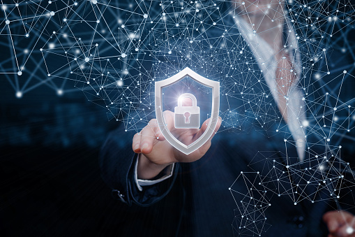 A businesswoman is touching a padlock inside a shield surrounded with digital system of wireless connections at dark blurred background.