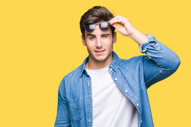 istock Young handsome man wearing sunglasses over isolated background winking looking at the camera with sexy expression, cheerful and happy face. 1097996352