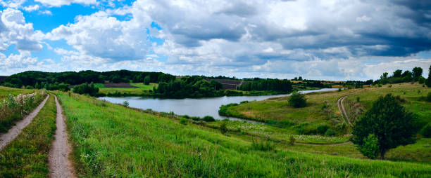 istock Cloudy windy summer panoramic landscape with country road and small river. 1098003050