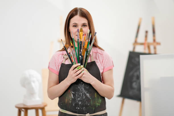 istock Young woman artist with brushes and paints in a white studio. 1098009244