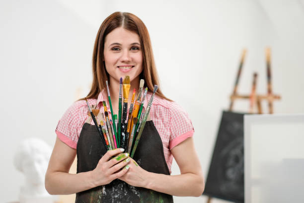 istock Young woman artist with brushes and paints in a white studio. 1098009348