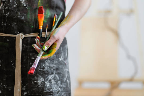vrouw artist's hand met een penseel en rode verf. zwarte schort, witte achtergrond. - beroep schilder vrouw stockfoto's en -beelden