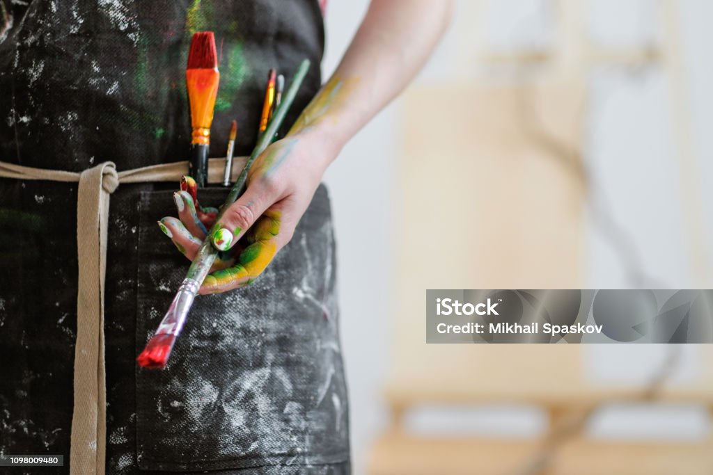 Woman artist's hand with a brush and red paint. Black apron, white background. Woman artist's hand with a brush and red paint. Black apron, white background in the art studio. Copy space. Artist Stock Photo