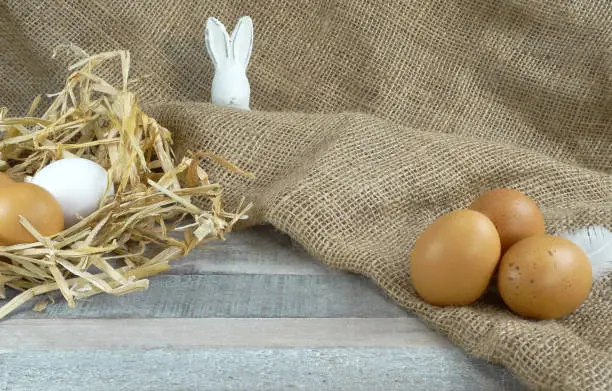 Chicken eggs in nest with burlap over wooden background