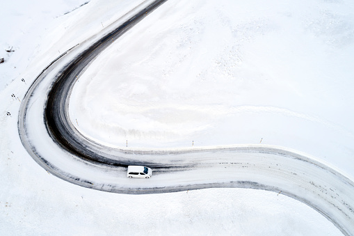 Aerial view of van vehice on snow covered mountain, winding road, Julier Pass, Swiss Alps.