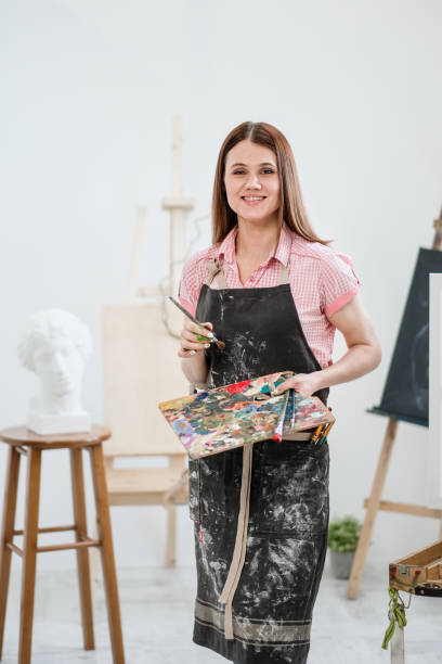 istock A young woman painter in a bright white studio draws a picture on canvas on an easel. 1098010266