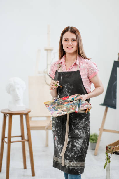 istock A young woman painter in a bright white studio draws a picture on canvas on an easel. 1098010374