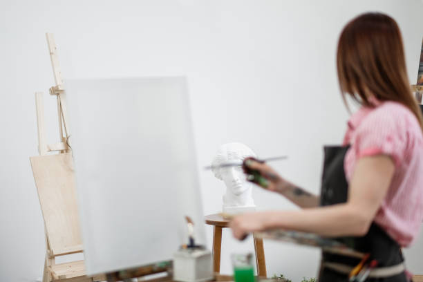 istock Young beautiful girl painter in a white studio draws on an easel on canvas. 1098011786