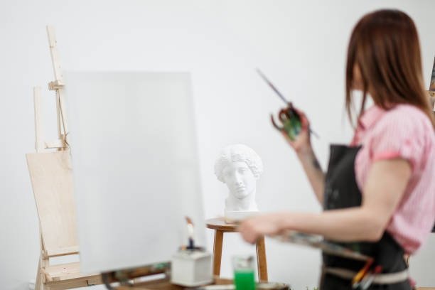 istock Young beautiful girl painter in a white studio draws on an easel on canvas. 1098011838