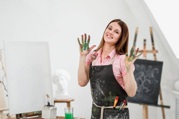 istock Young beautiful girl painter in a white studio with dirty palms shows class, laughs and rejoices. 1098012150