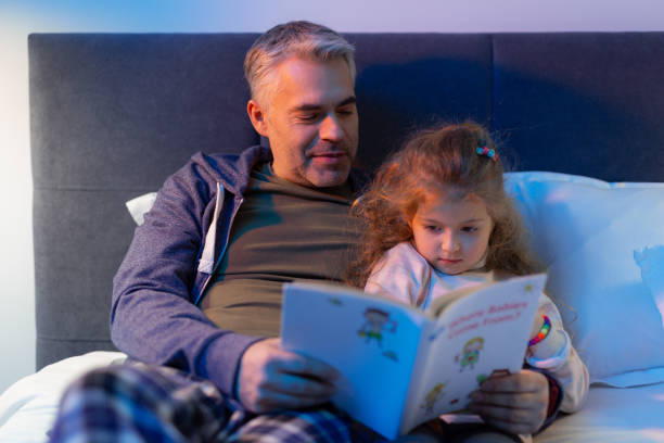 istock Bearded father reading a book to a small pretty long-haired daughter 1098031840