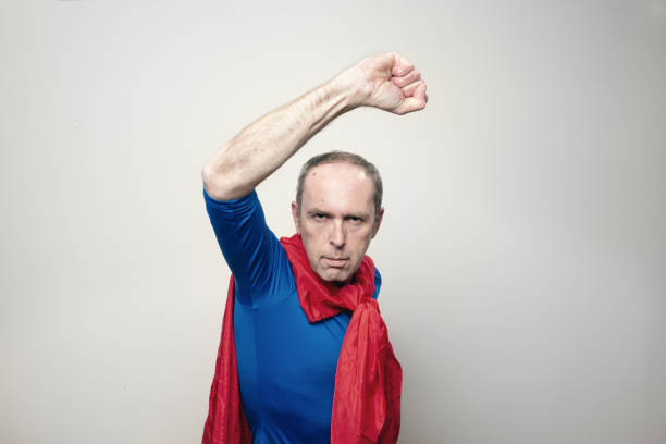 mature man, 53 years old, wearing a blue shirt and a red cape, posing as superman, raising a fist