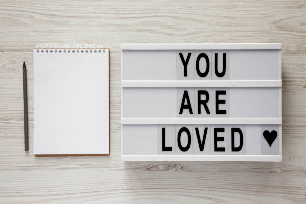 istock Lightbox with text 'You are loved', notepad and pencil on a white wooden background, top view. Flat lay, overhead. Valentine's Day 14 February. 1098038036