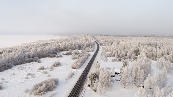 Drone point view, aerial view over the, frost covered landscape, very cold morning. frost covered forest, airy view of the landscape - forest, road and ice covered lake, country house in the foreground