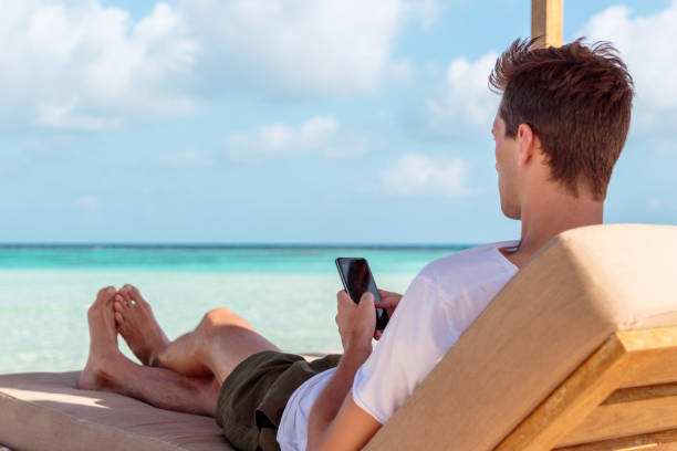 istock Man on a sunchair in a tropical location using his smartphone. Clear turquoise water as background 1098040718