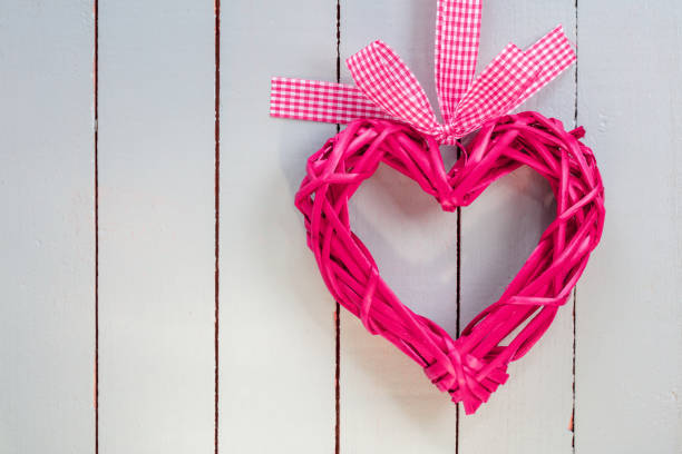 Pink heart hanging from pink ribbon on rose background. Horizontal composition with copy space. Valentine's Day concept.