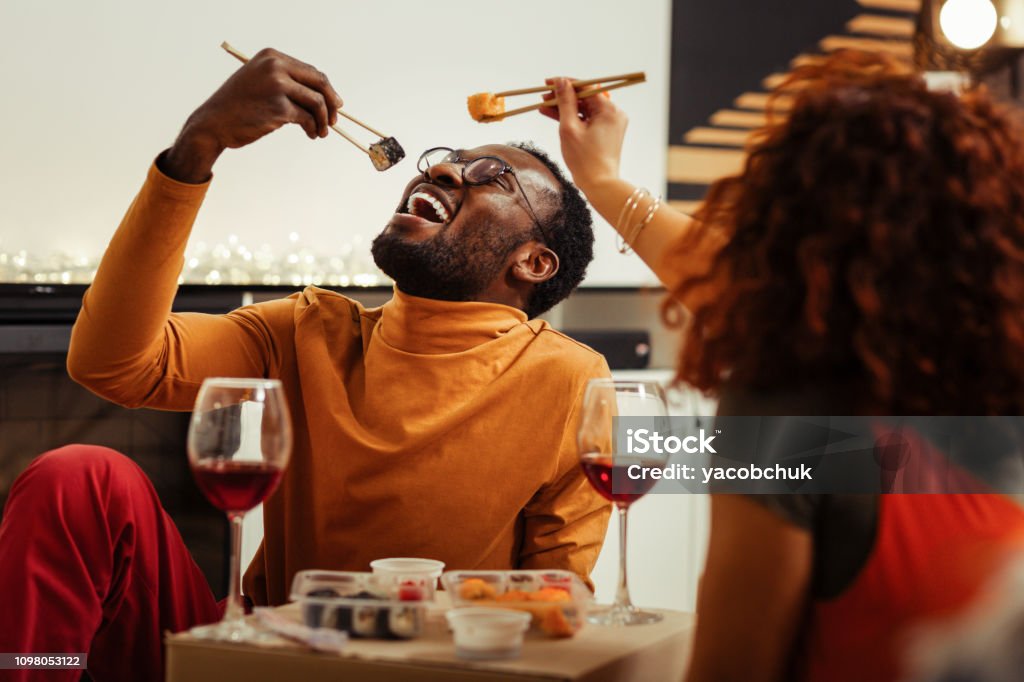 Couple having fun while eating sushi at home after fast delivery Having fun. Cute loving couple having fun while eating sushi at home after fast delivery Sushi Stock Photo