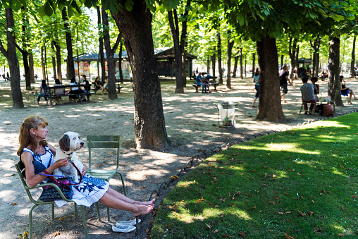 Paris, France - July 7, 2016: . Adult woman resting with dog in her lap at Le Jardin du Luxembourg, Paris, France. The Jardin du Luxembourg, or the Luxembourg Garden, located in the 6th arrondissement of Paris, was created beginning in 1612 by Marie de' Medici, the widow of King Henry IV of France, for a new residence she constructed, the Luxembourg Palace. The garden today is owned by the French Senate, which meets in the Palace.
