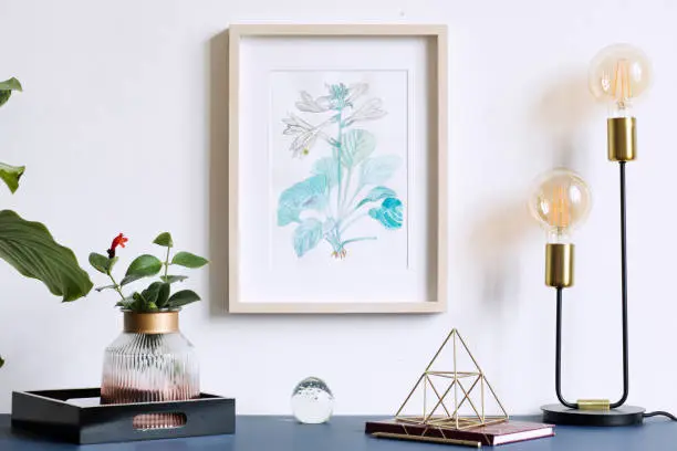 Photo of Home interior floral poster mock up with vertical wooden frame, table lamp, plants, accessories on the grey wall background. Concept with navy blue shelf.
