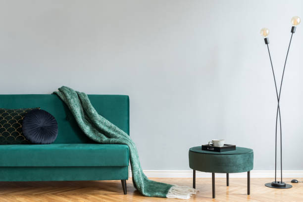 istock Minimalistic home interior with green velvet design sofa and pouf, black lamp and elegant blanket, pillows. Copy space for inscription, mock up poster. Brown wooden parquet. 1098076334