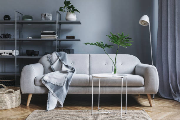 istock Modern nordic living room with design sofa with elegant blanket, coffee table,white lamp and bookstand on the grey wall. Brown wooden parquet. Concept of minimalistic interior. 1098077896