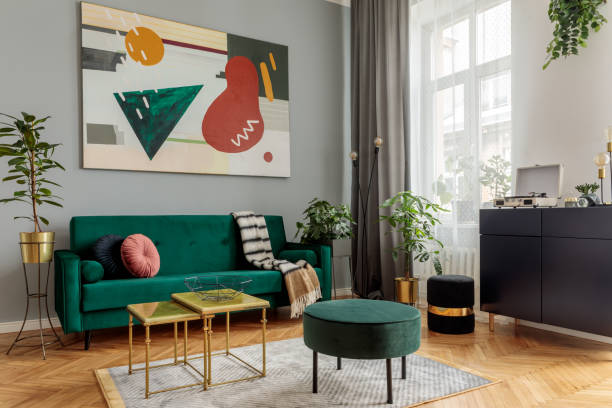 istock Luxury and modern home interior with design green sofa, navy commode, tables, pouf and accessroies. A lot of plants in the room. Abstract painting. Stylish decor of living room with brown parquet. 1098078842