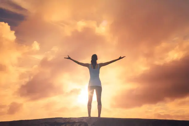 Photo of Woman raising arms in a beautiful sunset.