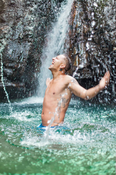 Imouzzer Ida Ou Tanane, Morocco, 08 14 2024 : Young Moroccan man jumping from a cliff into the water of a waterfall. Splash in the water. People watching.