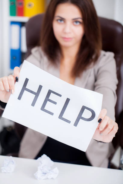 istock Stressed business woman imploring for help, holding a cardboard with the message Help . Focus is on the cardboard 1098110998
