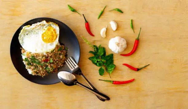 Photo of Salted pork with chili & Basil leaves in black plate on wood table, space for text input.