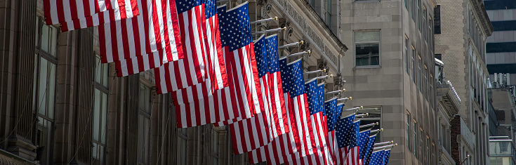 Multiple American flags blowing in the wind while hanging from buildings in New York.