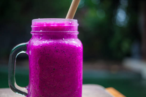 istock close up of passionfruit dragonfruit smoothie with eco friendly bamboo straw no plastic, glassware on a wooden board, condensation on the glass with a blue green pool background and wood elelents 1098149978