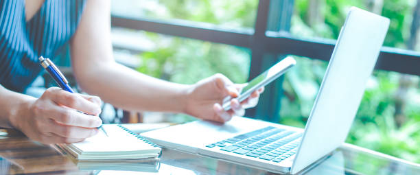 istock Business woman hand is writing on a notepad with a pen and using a mobile phone. 1098154192