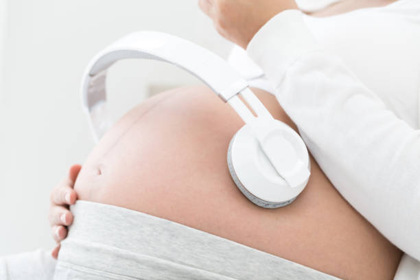 妊娠中の女性が胃に接続されているヘッドフォンを使用して胎児に良いモーツァルト効果音楽を聴いて、クラシック リラックス妊娠中に赤ちゃんのための音楽、胎児の発育のためのメロディ - home  audio ストックフォトと画像