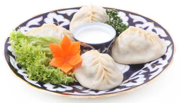 Uzbek manti with sour cream and herbs on a plate with an oriental ornament on a white background stock photo