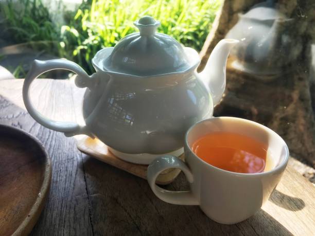 istock Herbal tea inside white cup and luxury white jar on wooden table. Both are put near glass wall with sunshine which reflect on another side. 1098195508
