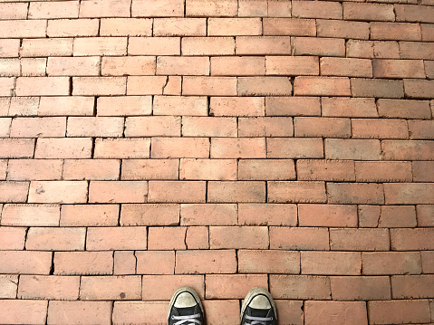 Gray sneakers standing on orange brick pavement texture floor