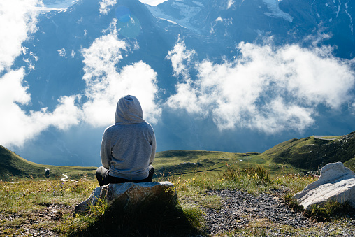 Young woman sitting looking at sea of clouds in mountain landscape. Rear view. Grossglockner, Austria.