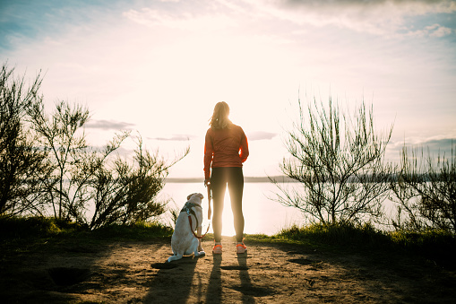 A young adult woman enjoys jogging outdoors on a beautiful day in the Pacific Northwest, her canine companion joining her for the exercise run.  Shot in Seattle, Washington.