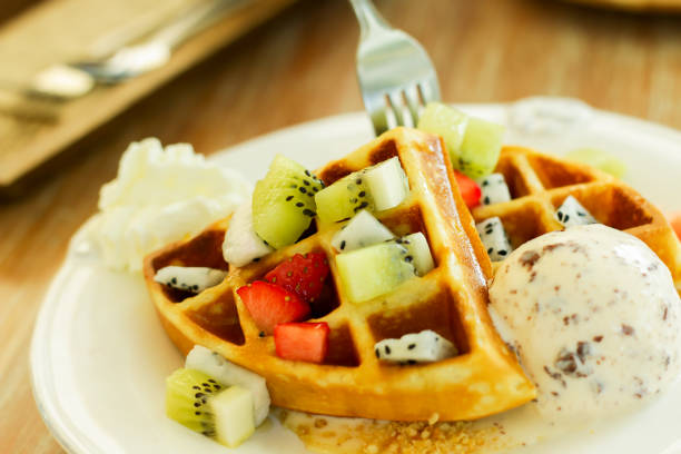 Waffle snacks, fresh fruit and ice cream in a white plate on a wooden table