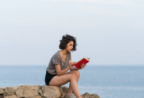istock Young woman sitting rocks reading a book 1098207618