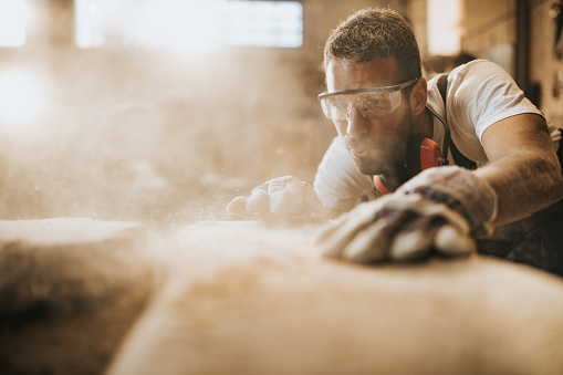 Young manual worker blowing sawdust from a wood at carpentry workshop.