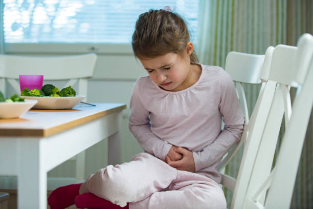 Child sitting at the table in the kitchen with stomach pain. stock photo