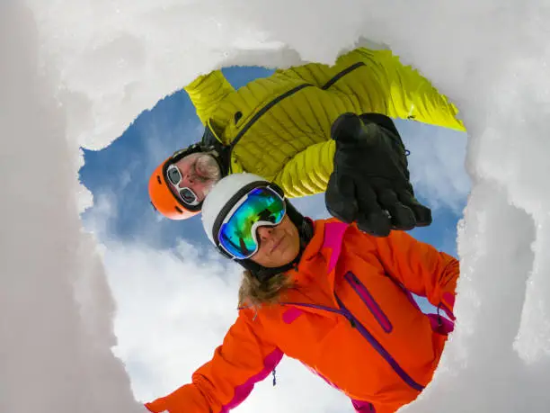 camera in snow hole - concept shot for avalanche rescue. Male and female skier in colorful winter clothes acting as montain rescue-service workers