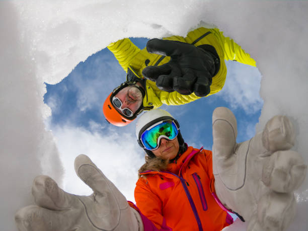 avalanche mountain rescue team reaching out helping hands in snow hole to save victim burried fisheye camera in snow hole - concept shot for avalanche rescue. Male and female skier in colorful winter clothes acting as montain rescue-service workers avalanche stock pictures, royalty-free photos & images