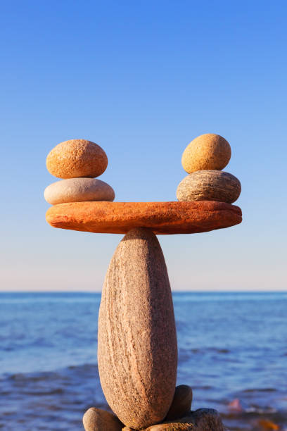 symbolic scales of the stones, illuminated by the evening sun, against the sea, close-up. pros and cons concept - balance simplicity nature beach imagens e fotografias de stock