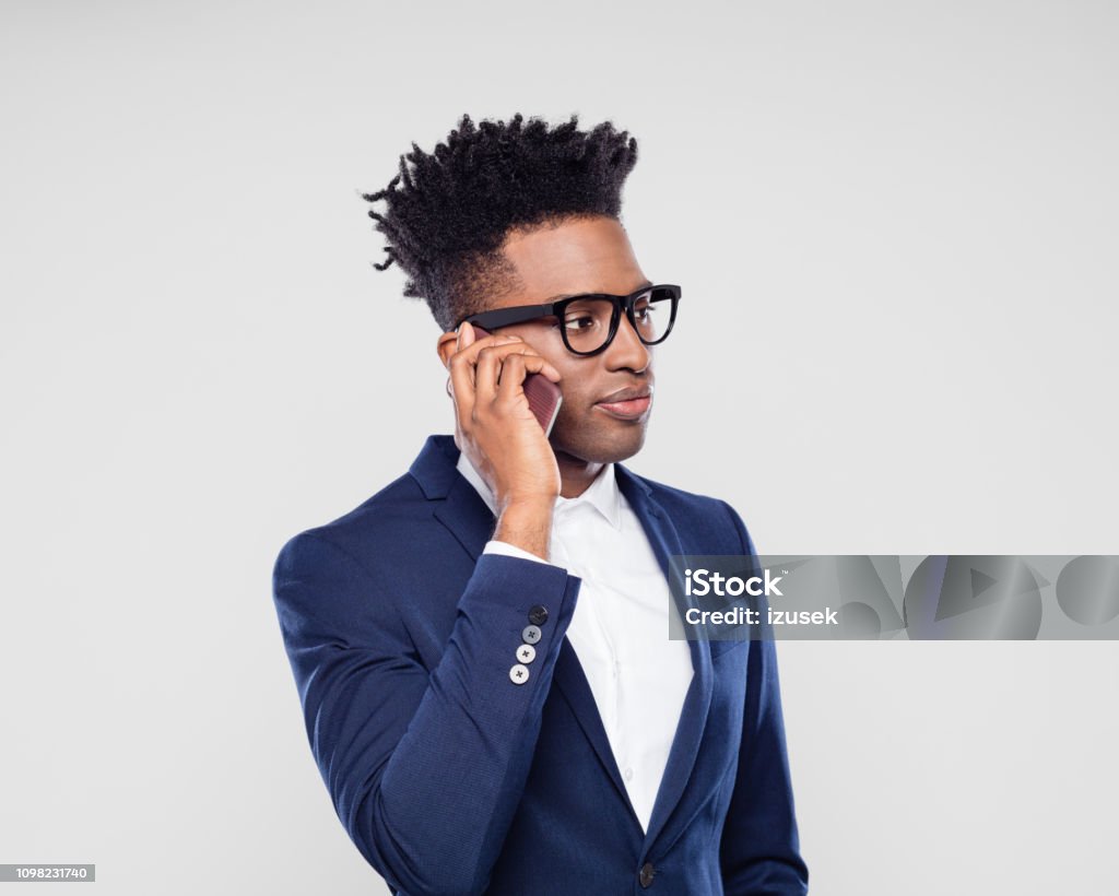 Black businessman talking on mobile phone Portrait of young black businessman talking on mobile phone against gray background African Ethnicity Stock Photo