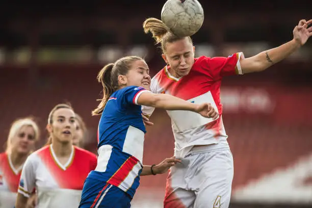 Determined teenage soccer players heading the ball on a match with their eyes closed.