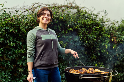 Cropped shot of a young woman tending to the barbecue outdoors